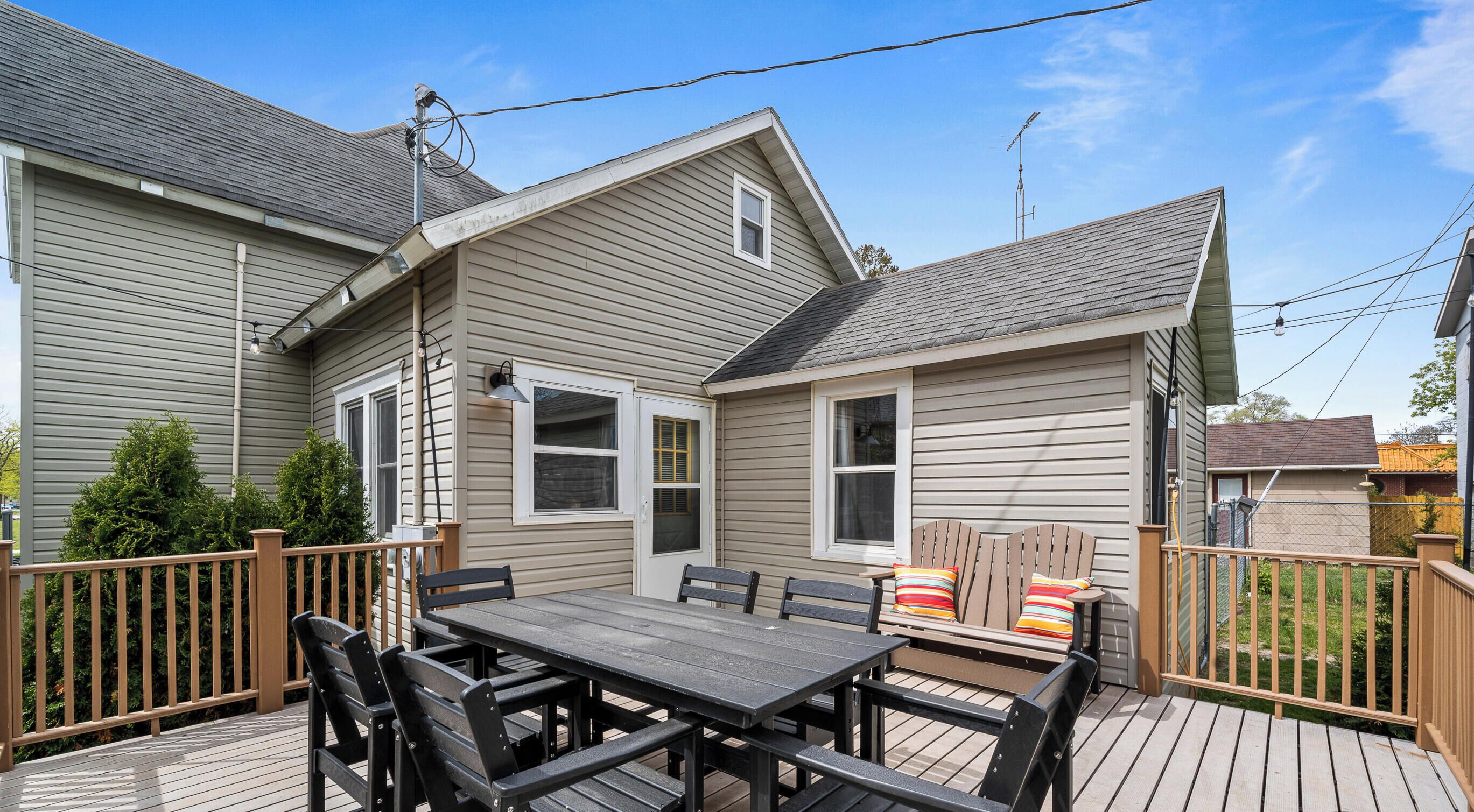Une terrasse avec une table et des chaises, une clôture en bois et une maison avec un toit et un revêtement de couleur grise.