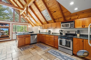 A spacious kitchen with wooden cabinets, a stainless steel stove, and a large window. - At Pond View, you can fish from the pond, soak in the hot tub, gather around the fire. (Twin Lakes)