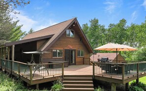 A wooden cabin with a deck, outdoor seating, and a grill area. - At Pond View, you can fish from the pond, soak in the hot tub, gather around the fire. (Twin Lakes)