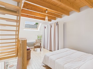Ein Schlafzimmer mit Holzbalkendecke, einem Bett, einem Stuhl, einem Fenster und einem Oberlicht.