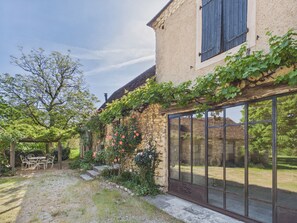 Ein Steinhaus mit Garten, einer Pergola und einem großen Fenster.