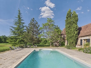 Ein Pool mit Liegestühlen, umgeben von Bäumen und einem Steinhaus.