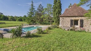 Uma casa de pedra com piscina, rodeada por vegetação e árvores.