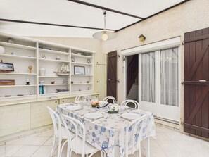 Eine überdachte Terrasse mit Esstisch, umgeben von weißen Stühlen und einem Regal mit verschiedenen Dekorationsgegenständen.