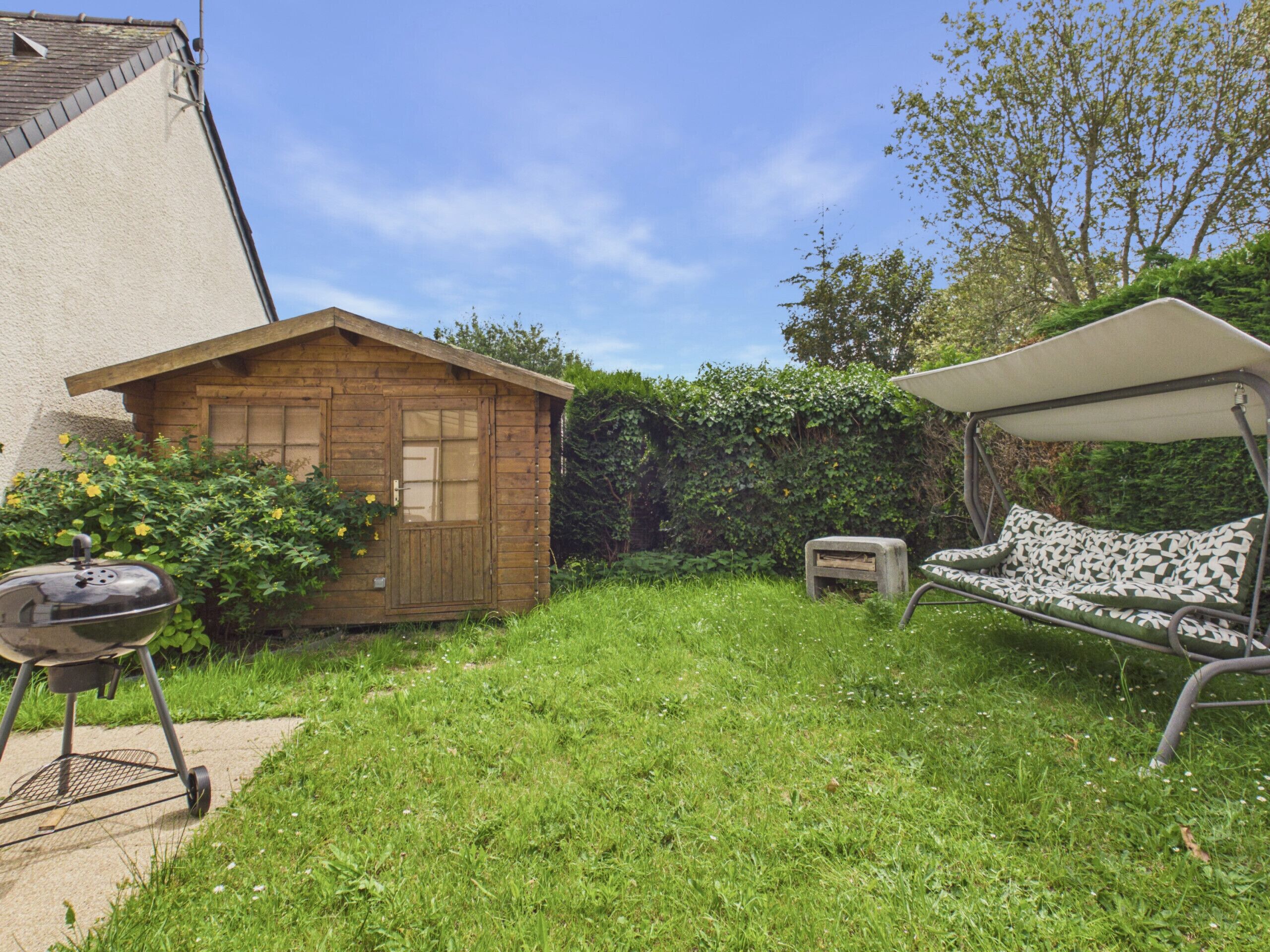 Ein Garten mit einem Holzschuppen, einem Grill, einer Schaukel und einer überdachten Sitzgelegenheit.