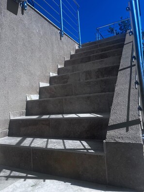 Un escalier extérieur en pierre, agrémenté de rampes métalliques, menant à l’entrée d’un bâtiment.