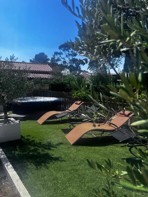 Une terrasse avec deux chaises longues, un petit arbre et, au fond, un bâtiment doté d’un toit recouvert de tuiles.