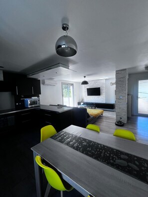 Een moderne keuken met een magnetron, een zithoek met een tafel en stoelen, een bank en een aan de muur bevestigde televisie.
