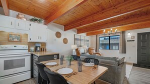 Et moderne køkken med hvide skabe, et spisebord dækket til fire personer, og en grå sofa i opholdsstuen.