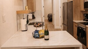 Una cucina moderna con isola in marmo, due sgabelli da bar, mobili in legno, elettrodomestici in acciaio inossidabile e illuminazione a sospensione.