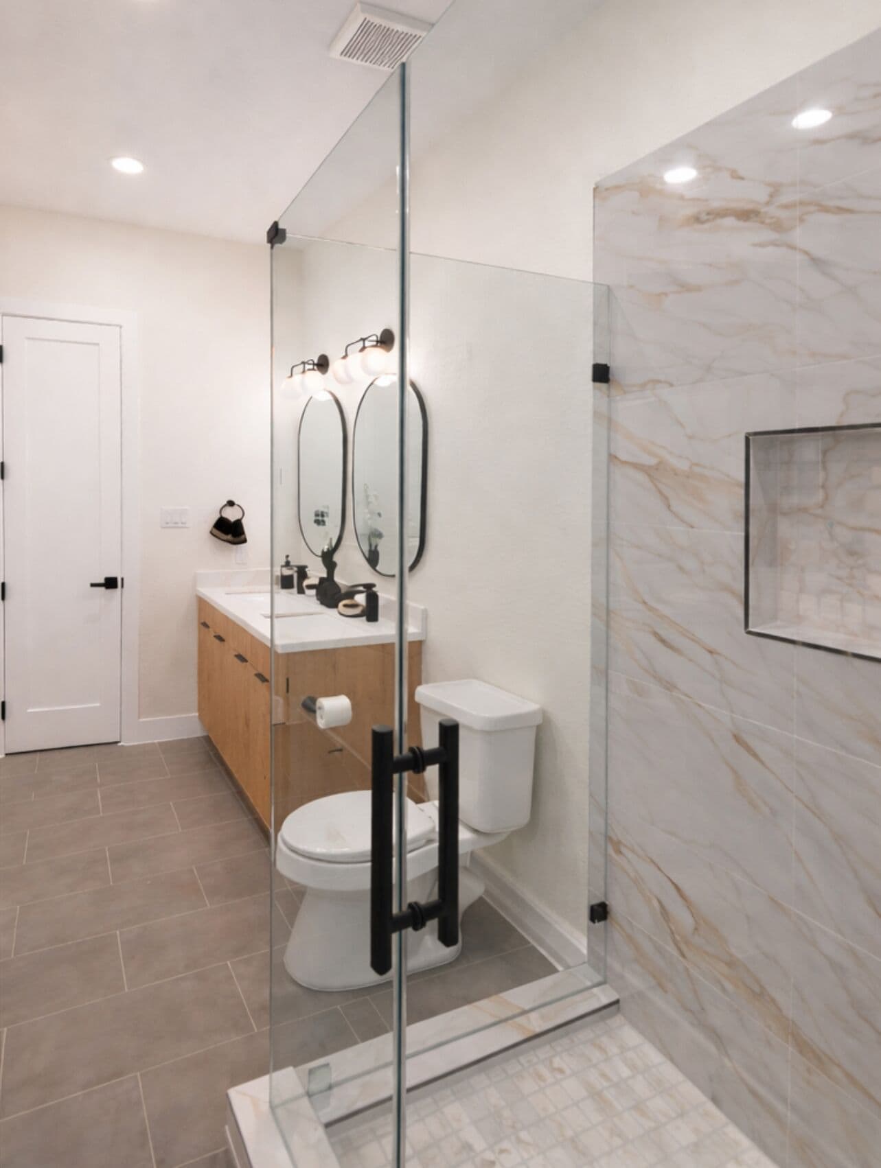 A modern bathroom with a glass-enclosed shower, a toilet, and a vanity with a mirror.