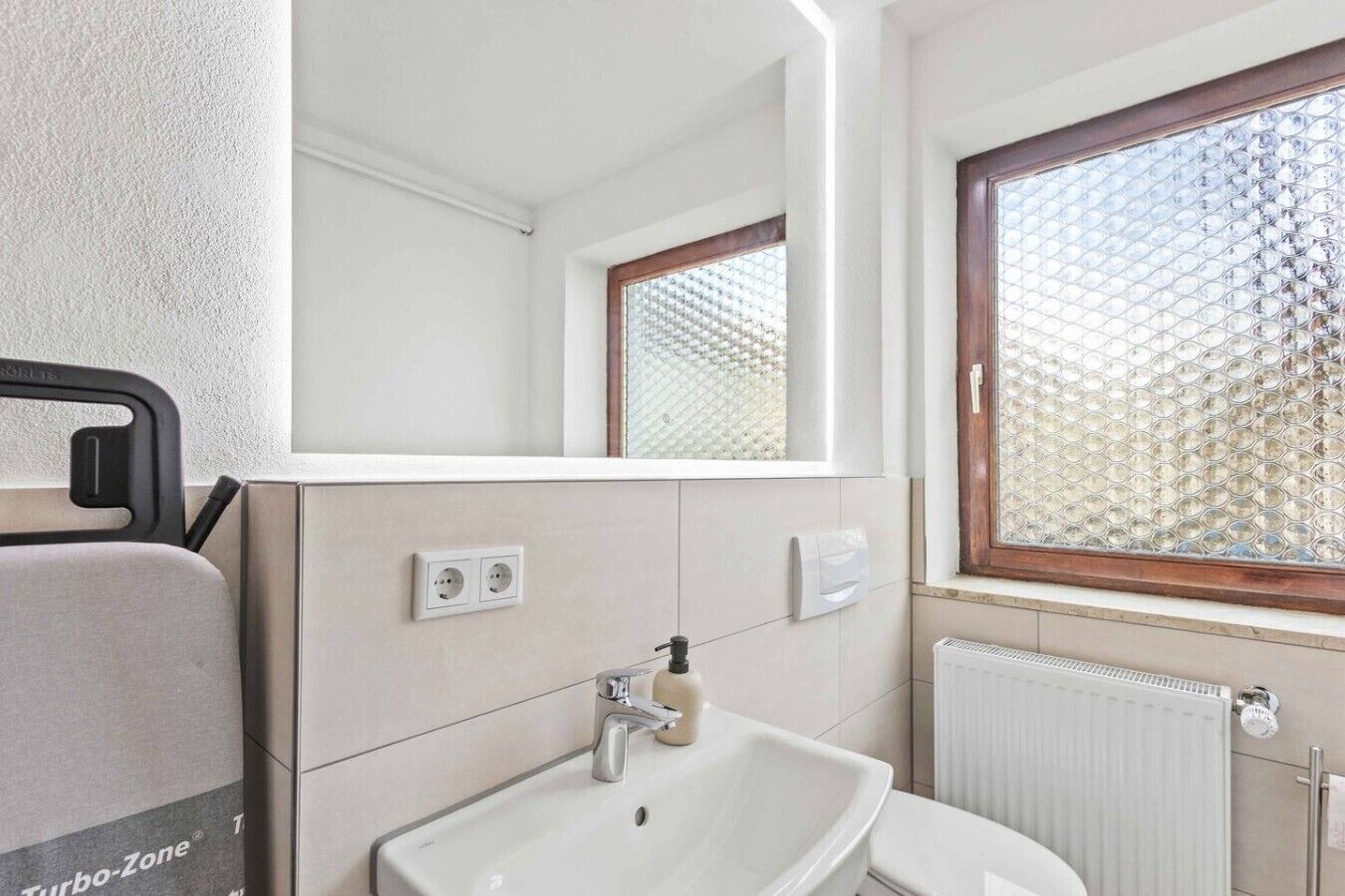 A bathroom with a sink, mirror, window, and radiator.
