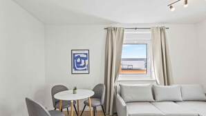 En moderne stue med sofa, to stole, et lille bord, en potteplante og et vindue med gardiner.