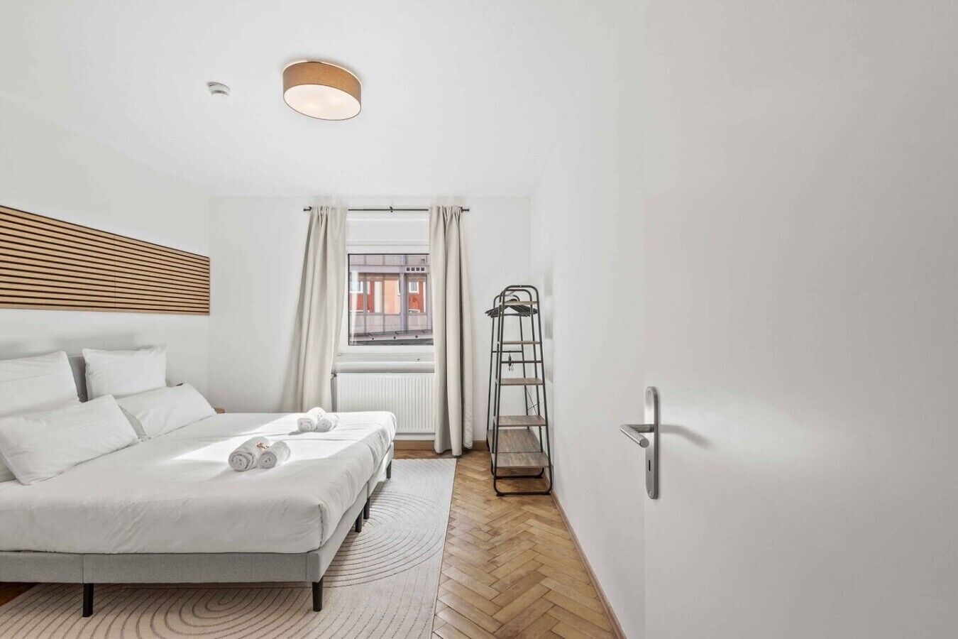 A modern bedroom with a bed, a window with curtains, a radiator, and a metal ladder.