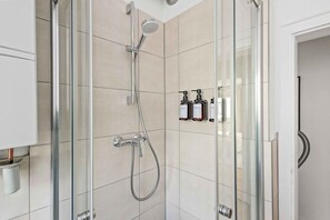Eine moderne Dusche mit Handbrause und Wandarmatur, eine Glastrennwand und eine kleine Ablage mit Pflegeprodukten.