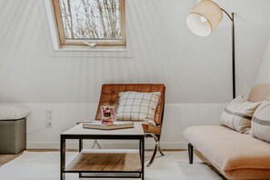 Ein Zimmer mit Fenster, einem Sessel, einer Couch, einem Couchtisch und einer Stehlampe.
