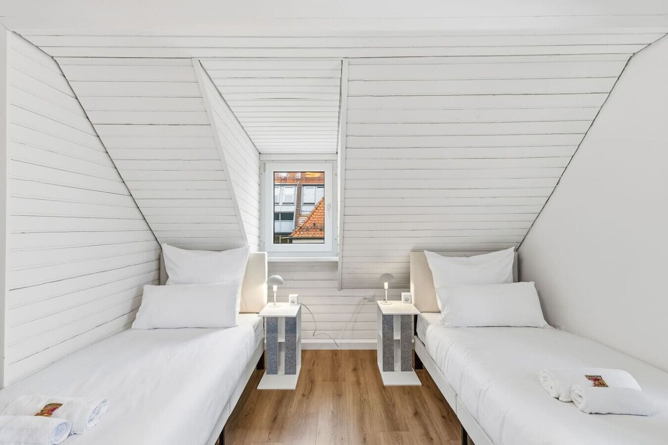 Une chambre avec deux lits, une fenêtre donnant sur des immeubles et un plancher en bois.