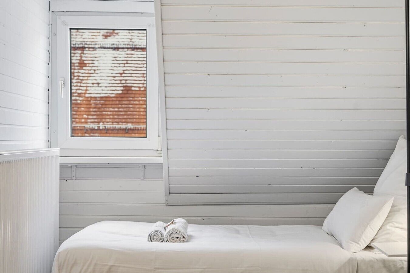 Een slaapkamer met een raam, een bed en een radiator.