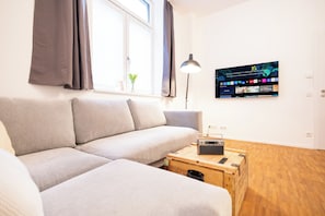 Un saló modern amb un sofà, una taula de centre de fusta, una làmpada i un televisor fixat a la paret.