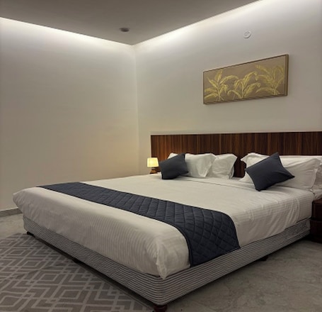A large bed with a quilted headboard, a bedside table with a lamp, and a wall-mounted artwork.. Fairy heights