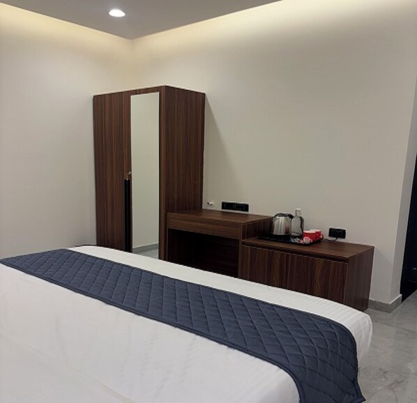 A hotel room with a bed, a wardrobe, a desk with a kettle, and a coffee maker. - Fairy heights  (Kodaikanal)