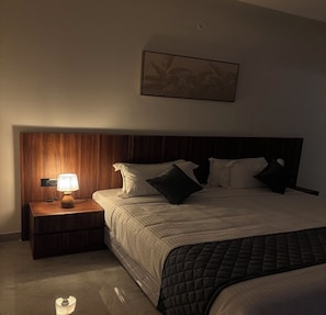 A bedroom with a wooden headboard, a bedside table with a lamp, a bed with pillows, and a framed picture on the wall.