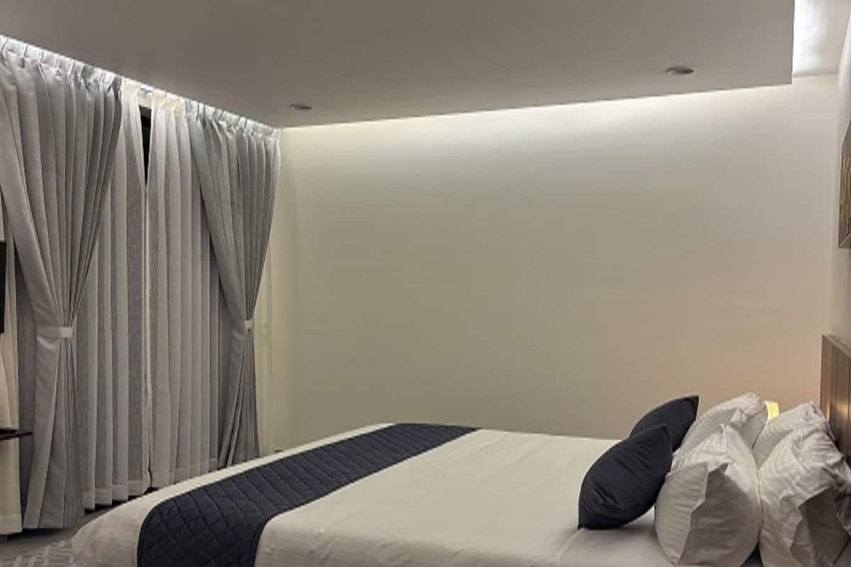 A modern bedroom with a large bed, a wooden headboard, and a window with curtains.