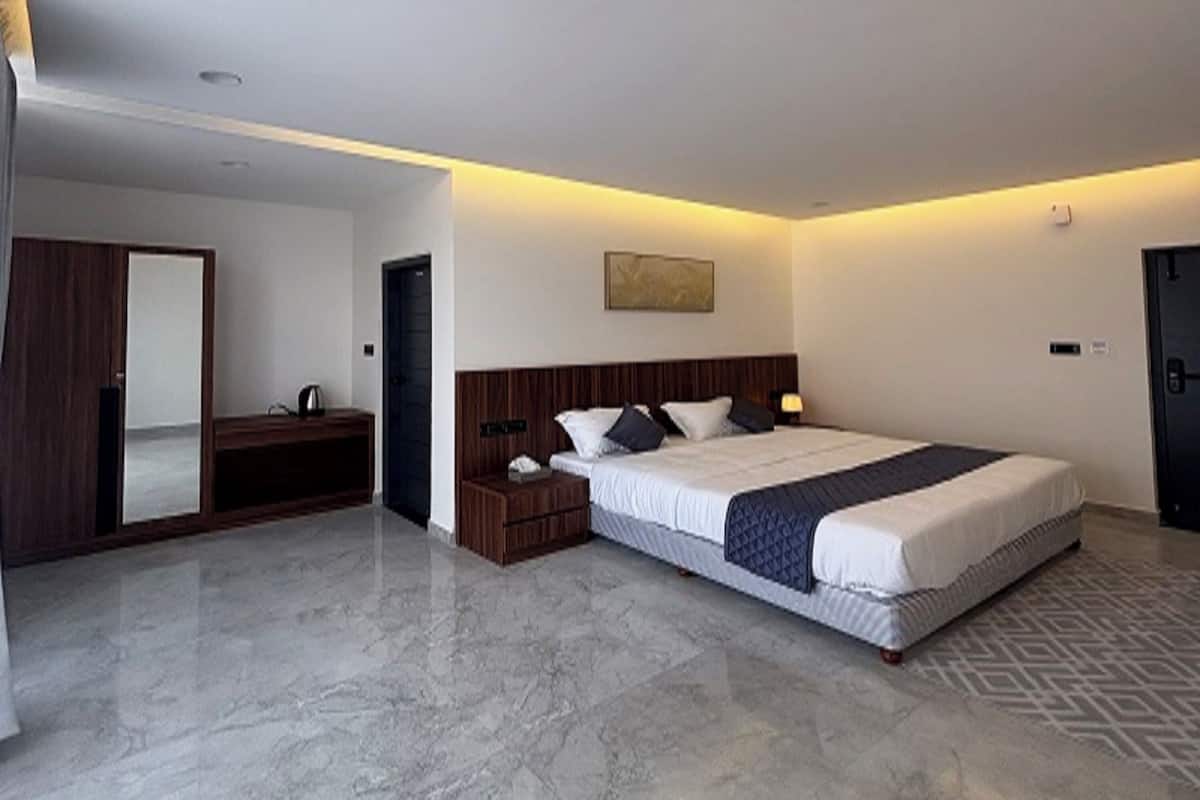 A modern hotel room with a large bed, a wooden nightstand, a mirror, and a door.