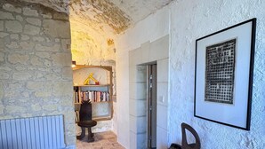 A room with a stone wall, a wooden cabinet, a radiator, and a bookshelf. - Family suite in troglodyte house with access to indoor swimming pool (La Roche-Clermault)
