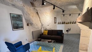 A room with a stone ceiling, a brown sofa, a blue chair, a yellow chair, and a patterned rug. - Family suite in troglodyte house with access to indoor swimming pool (La Roche-Clermault)