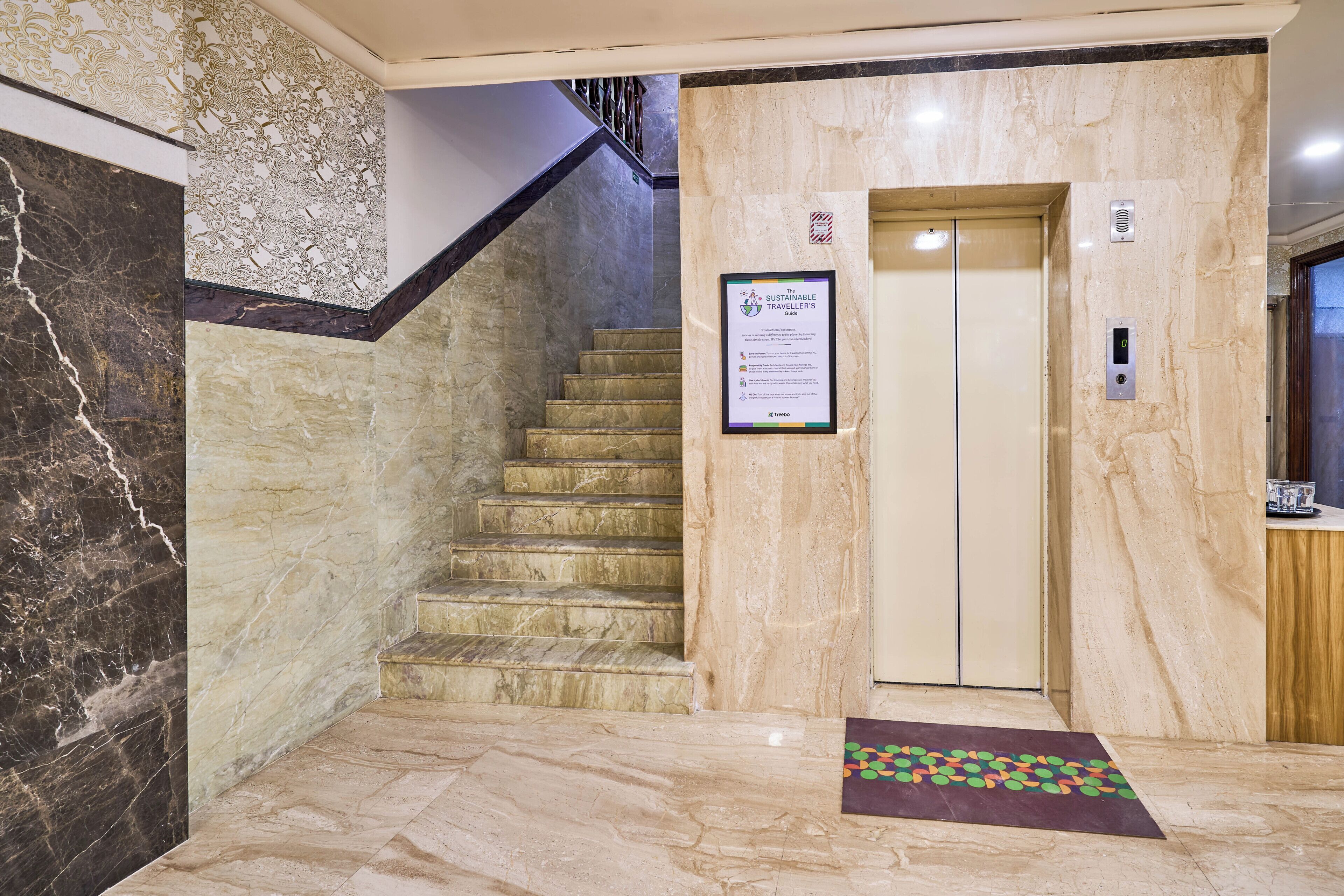 A marble-floored lobby with a staircase, an elevator, and a sign about sustainable projects.
