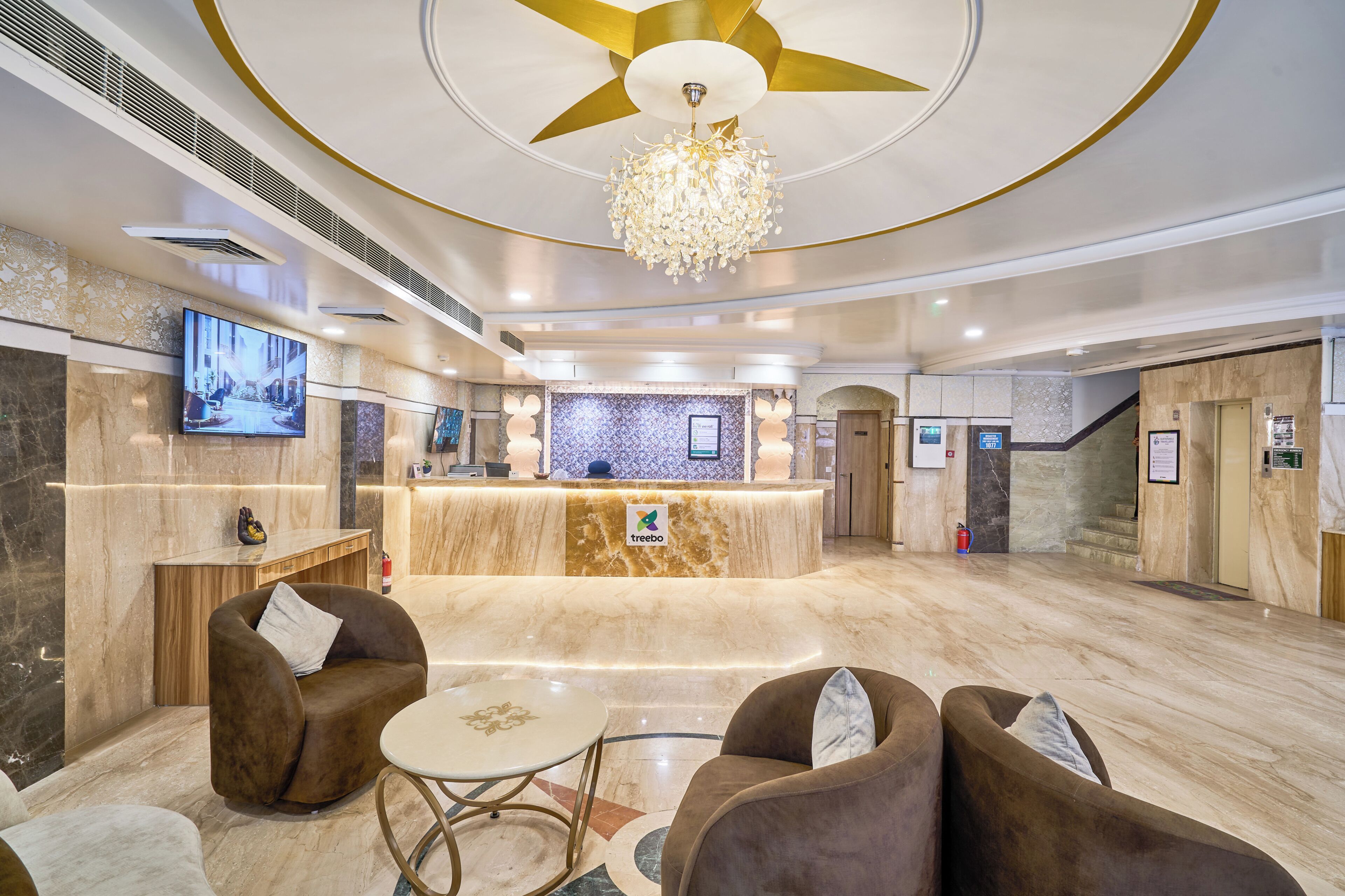 A hotel lobby with a reception desk, comfortable seating, a chandelier, and a large TV screen.
