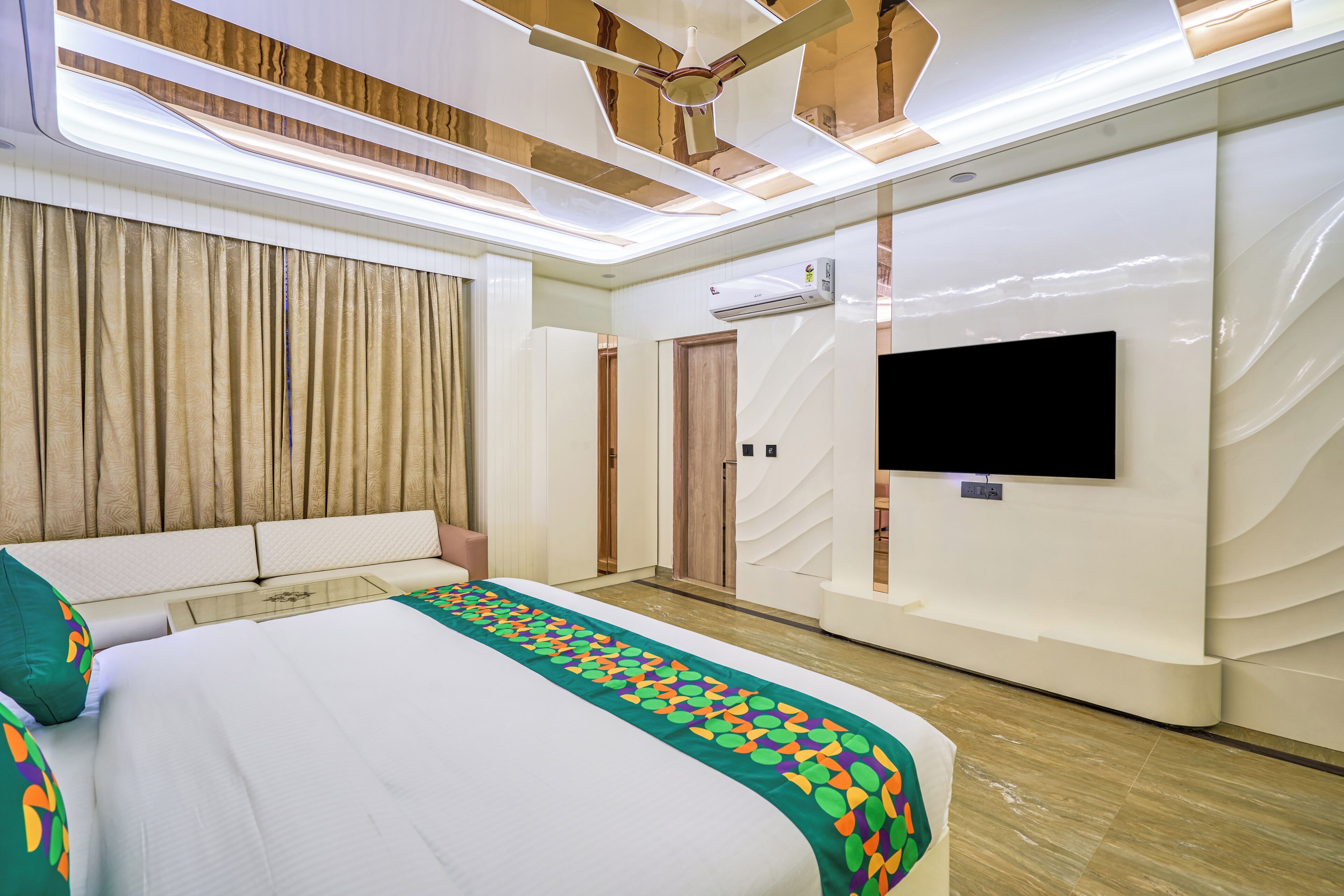 A modern hotel room with a large bed, a flat-screen TV, a ceiling fan, and an air conditioning unit.