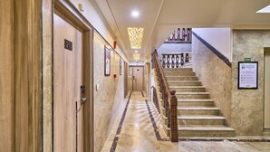 A hotel hallway with marble flooring, wooden doors, and a staircase with a wooden railing.