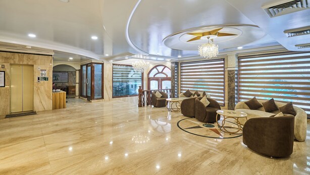 A spacious lobby with a marble floor, a reception desk, a chandelier, and a seating area with sofas and a coffee table.