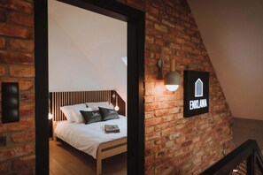 Une chambre avec un mur en briques, un lit recouvert de draps blancs et un panneau indiquant « ENKLAVA ».