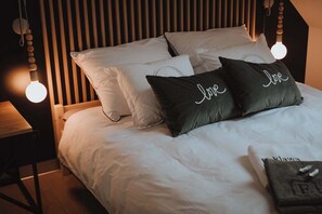 A neatly made bed with white bedding and two dark pillows with the word 'Love' on them.