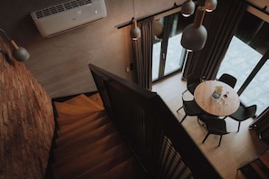 Un intérieur moderne avec un escalier, un coin repas comprenant une table ronde et des chaises, et une grande fenêtre avec des rideaux.