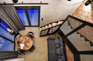 A modern interior with a round wooden table, grey sofa, and a staircase with a mesh railing.