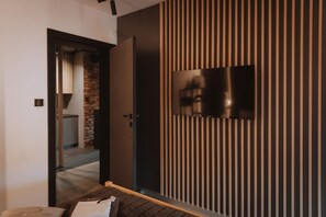 Une chambre moderne Ă©quipĂ©e dâun lit, dâun tĂ©lĂ©viseur fixĂ© au mur et dâune porte donnant sur une autre piĂšce.