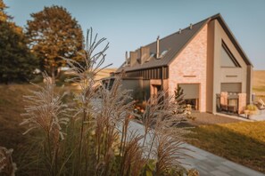 Une maison moderne avec une façade en pierre, un toit en pente et un espace extérieur aménagé pour se détendre.