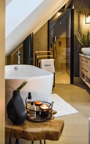 A modern bathroom with a large bathtub, a wooden chair, a towel rack, and a small table with candles.