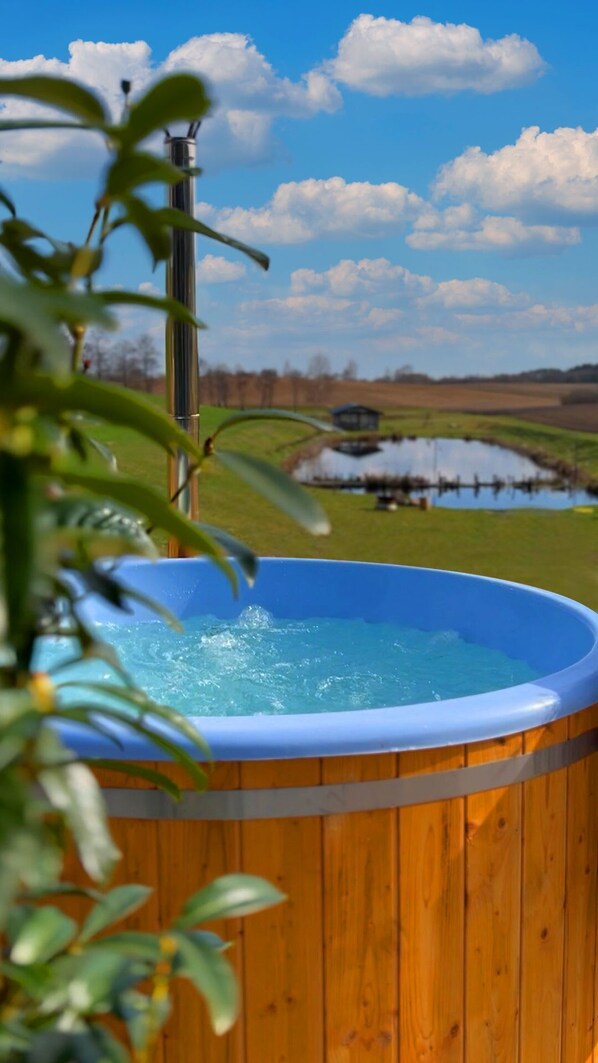 A wooden hot tub with a clear view of a pond and trees in the background.