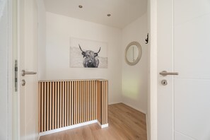 A hallway with a wooden slatted partition, a round mirror on the wall, and a black and white artwork of a bull. - Holiday Home “Häusle Felix” with Private Terrace, Shared Garden, and Wi-Fi (Ottersweier)