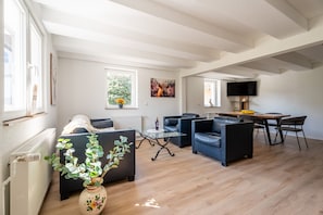 Un salon moderne comprenant un canapé, des fauteuils, une table basse en verre et un coin repas avec un téléviseur et une table.