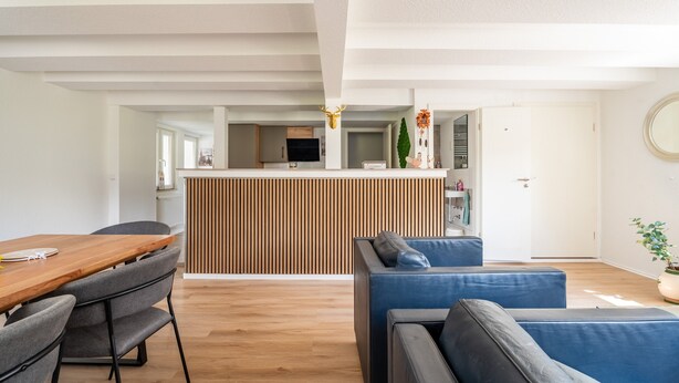 Un salon moderne avec une table à manger en bois, des canapés gris et une cuisine en arrière-plan.
