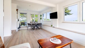 Un interior moderno con comedor, televisor montado en la pared y ventanas amplias.