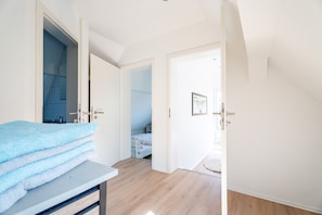 Una stanza con un letto, un bagno con doccia blu e un corridoio che porta a un'altra stanza.