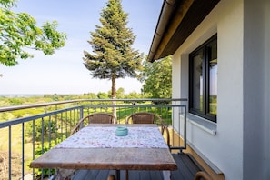 Un balcone con tavolo e sedie, affacciato su un paesaggio con alberi e una vista lontana.