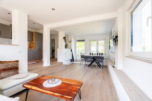 A modern living room with a wooden coffee table, a sofa, and a dining area with chairs.